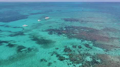 A-4K-drone-shot-of-boats-floating-in-crystal-clear-blue-water-of-the-Caribbean-Sea,-near-Bimini,-Bahamas