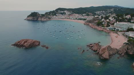 A-sweeping-aerial-pan-of-Tossa-del-Mar-in-Costa-Brava,-Spain-with-boats-in-the-harbor-and-the-city-full-of-life