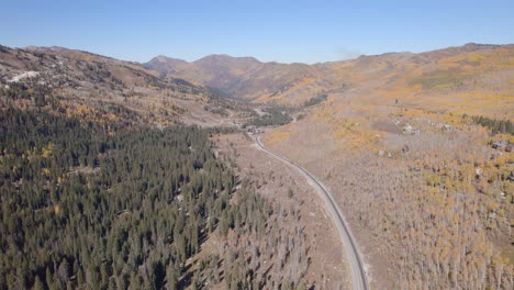 Wide-open-aerial-shot-that-follows-along-a-valley-and-a-road-through-Utah-during-the-autumn-daytime