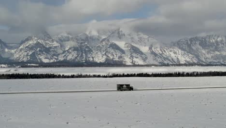 A-4K-drone-shot-of-a-truck-driving-on-a-remote-road-with-the-largest-and-tallest-peaks-of-the-Teton-Range-dominating-the-background,-in-Grand-Teton-National-Park-in-Northwestern-Wyoming