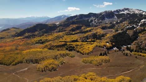 A-high-altitude-aerial-shot-of-hiking-trails-surrounded-by-snowcapped-mountains-and-yellow-aspens-in-Utah-during-the-autumn