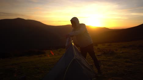 Backpacking-man-preparing-pitching-camping-tent-in-sunset-wilderness
