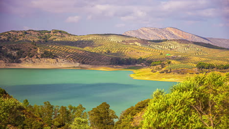 Timelapse-shot-of-cloud-movement-over-El-Limonero-reservoir,-surrounded-green-countryside-along-hilly-terrain-in-Malaga,-Spain