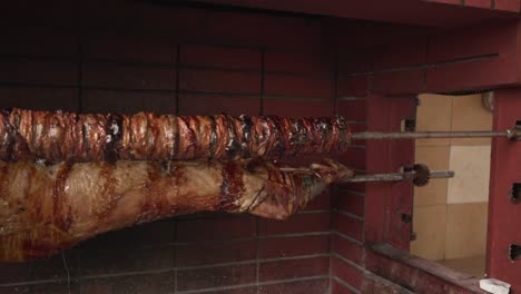 Front-view-of-traditional-kokoretsi-and-lamb-spits-over-charcoal,-turning-on-electric-barbecue,-PAN-shot-4K