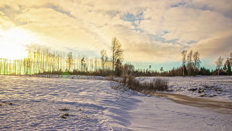 Zeitrafferaufnahme-Von-Weißen-Wolken,-Die-An-Einem-Kalten-Wintermorgen-über-Schneebedecktes-Ackerland-Ziehen,-Mit-Aufgehender-Sonne-Im-Hintergrund
