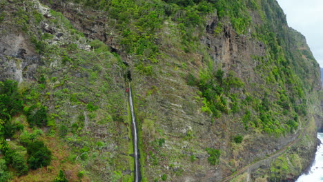 Cascada-En-Un-Acantilado-En-Madeira-Con-Un-Escalador-Oceánico-Con-Drones-Disparado-Olas-Panorámicas-Mar-Nublado