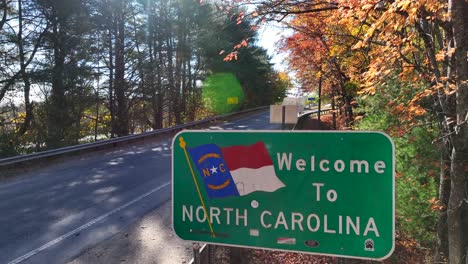 Welcome-to-North-Carolina-sign-along-winding-road-lined-by-colorful-trees-in-autumn