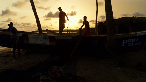 Silhouette-Eines-Schwarzen-Mannes-Bei-Sonnenuntergang,-Der-An-Einem-Fischerboot-Am-Tropischen-Strand-Arbeitet