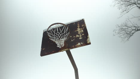 Old,-rusty-basketball-hoop-with-slow-motion-snowflakes-falling-during-winter-snow-storm