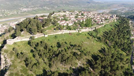 Drone-view-in-Albania-flying-in-Berat-town-over-a-medieval-castle-on-high-ground-fort-showing-the-brick-brown-roof-houses-from-top