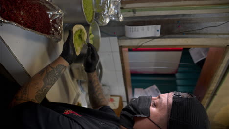 Slow-motion-vertical-close-up-of-a-man-with-black-latex-gloves-spreading-guacamole-on-a-tortilla-in-a-traditional-mexican-restaurant