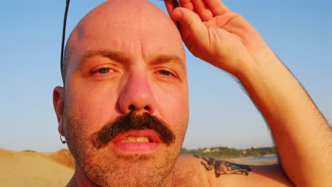 Kaukasischer-Männlicher-Kahler-Alopezie-Mit-Schnurrbart-Und-Sonnenbrille-Am-Strand-Bei-Sonnenuntergang