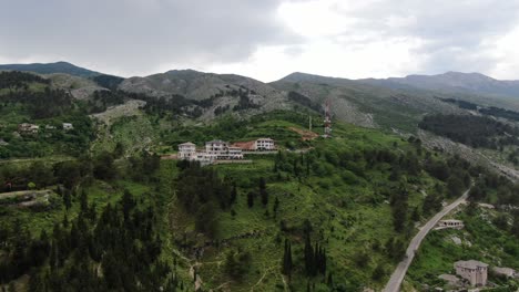 Drohnenansicht-In-Albanien,-Die-In-Gjirokaster-über-Eine-Mittelalterliche-Stadt-Fliegt-Und-Einen-Grünen-Berg-Mit-Einem-Hotel-Und-Häusern-Mit-Braunem-Backsteindach-Zeigt