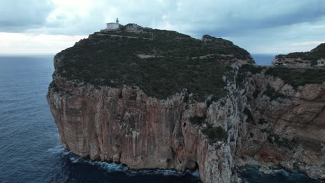 Capo-Caccia,-Sardinia:-close-orbit-aerial-view-of-the-lighthouse-and-cliff-of-this-famous-cape-on-the-island-of-Sardinia-during-sunset