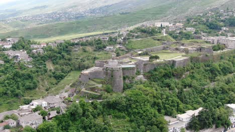 Drone-view-in-Albania-flying-in-Gjirokaster-town-over-a-medieval-castle-on-high-ground-fort-showing-the-brick-brown-roof-houses