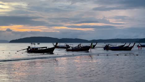 Long-Tail-Boats-ferrying-people-to-the-shore,-silhouetted-against-a-captivating-evening-sky