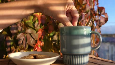 Woman-dipping-biscuits-into-hot-drink-with-colorful-autumn-leaves-in-background