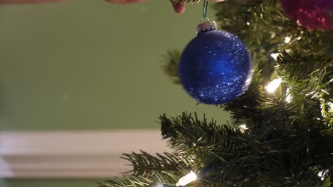 Person-Puts-Up-a-Sparkling-Ornament-on-the-Christmas-Tree,-Side-View