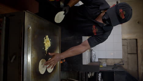 Vertical-slow-motion-of-a-cook-placing-some-tortillas-next-to-grilling-cheese-on-a-griddle-at-a-restaurant-in-Mexico