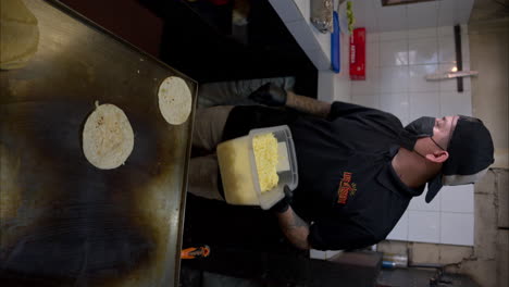 Vertical-slow-motion-of-a-male-latin-cook-grilling-cheese-on-a-griddle-and-placing-a-tortilla-on-top-to-prepare-a-quesadilla-in-a-mexican-restaurant