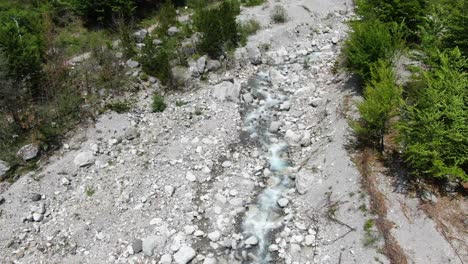 Vista-De-Drones-En-Albania-En-Los-Alpes-Volando-Sobre-Un-Río-Cristalino-Con-Suelo-Rocoso-Con-Bosque-Verde-A-Los-Lados-En-El