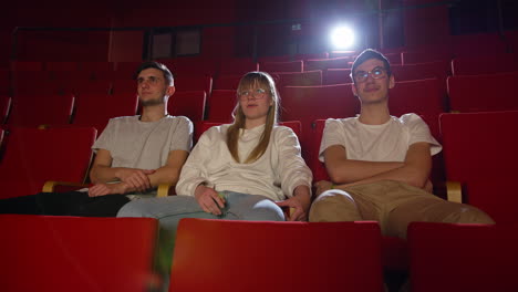 Nervous-girl-sitting-between-two-boys-in-the-cinema-auditorium,-handheld-shot