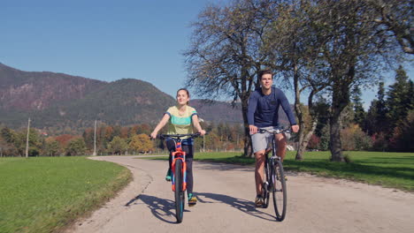 Woman-and-man-riding-bikes-and-enjoying-nature-on-a-fall-sunny-day,-front-view
