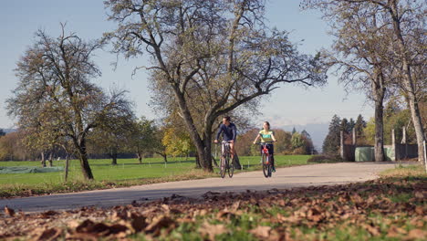 Cycling-couple-enjoying-a-ride-at-the-park-in-the-autumn-season,-wide-shot