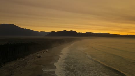 Stunning-golden-sunset-above-Bruce-Bay-with-waves-hitting-shore,-aerial