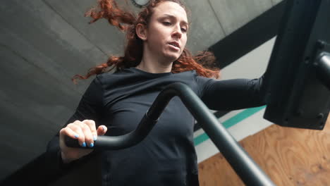 Red-haired-woman's-intense-CrossFit-training-on-an-air-bike-in-a-close-up,-slow-motion-shot