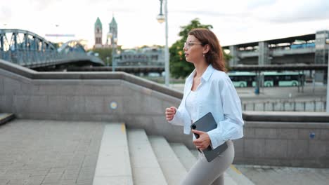 Modern-young-businesswoman-with-tablet-purposefully-walking-up-steps-against-urban-background,-concept-career-advancement-female-empowerment