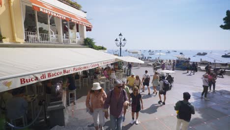 Amalfi-Positano-Italy-Immersive-Travel-Tourism-Mediterranean-Sea-Coast-Water-Europe,-Walking,-4K-|-Beautiful-Woman-with-Tattoos-Passing-Near-Iconic-Crowded-Plaza