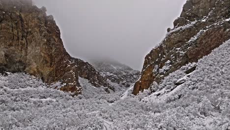 Cinematic-aerial-dolly-tilts-up-to-reveal-epic-brown-quartz-rock-cliffs-covered-in-snow,-Rock-Canyon-Utah