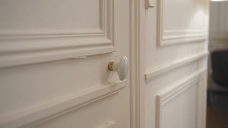 Close-up-shot-of-female-hands-rotating-door-knob-before-opening-a-white-door-in-a-house