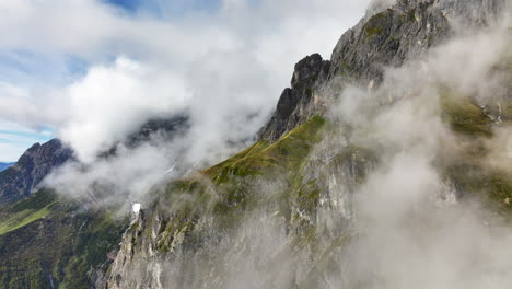 Beautiful-ascending-drone-shot-of-rocky-mountain-side-in-Austrian-Alps-through-misty-clouds