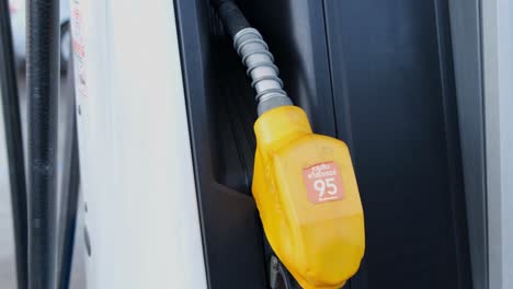 A-yellow-fuel-nozzle-revealed-in-a-rest-position-on-gas-station-as-the-camera-zooms-out,-Thailand
