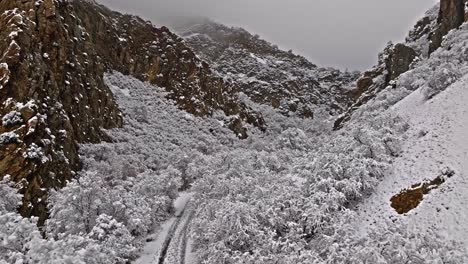 Aerial-trucking-pan-establish-mouth-of-large-quartz-canyon-with-trees-and-rocks-covered-in-snow
