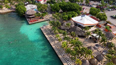 Aerial-parallax-around-clear-turquoise-Caribbean-waters-by-Jan-Thiel-and-Zanzibar-beach-resorts,-Curacao