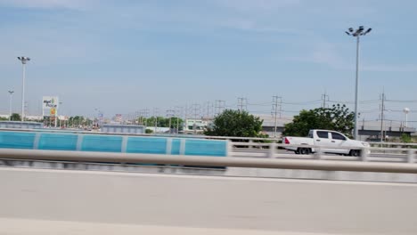 Two-white-cars-then-another-white-truck-followed-by-the-camera-as-urban-communities-are-seen-with-electric-posts-and-the-blue-sky,-Kanchanaphisek-Road,-Thailand