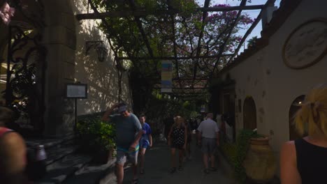 Amalfi-Positano-Italy-Immersive-Travel-Tourism-Mediterranean-Sea-Coast-Water-Europe,-Walking,-4K-|-Moving-Towards-Artistic-Green-Vines-in-Alley-Behind-Woman-in-Black-Dress,-Shaky