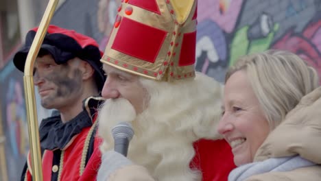 Sinterklaas-Hablando-Por-El-Micrófono-De-Cerca-Con-Pete-En-Segundo-Plano,-Portátil
