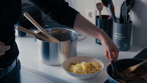 Young-woman-putting-meat-sauce-from-Pan-onto-the-Tagliatelle-Pasta-in-a-Plate-in-white-kitchen-during-a-day-in-slow-motion