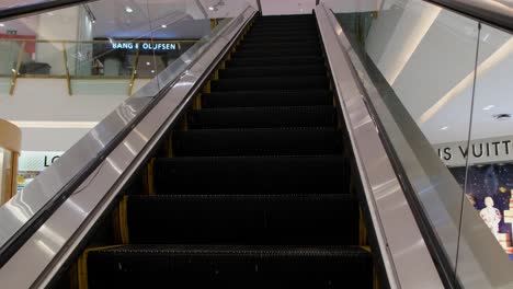 BANG-and-OLUFSEN-on-the-left-and-LOUIS-VUITTON-on-the-right-revealed-while-going-up-an-escalator-in-Emprium-mall-down-Sukhumvit,-Bangkok,-Thailand