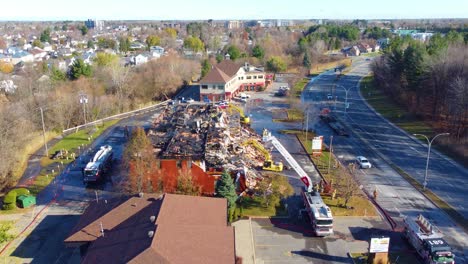 Drone-view-of-a-garage-building-that-was-badly-burned-being-cleaned-by-the-local-fire-department-using-heavy-equipment