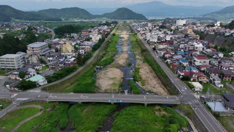 Yamanochi-town-and-Yomase-river,-summer-in-Japan---descending-tilt-drone-shot