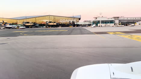 Blick-Aus-Einem-Flugzeugfenster-Auf-Das-Rollfeld,-Sonnenaufgang-Am-Flughafen,-Flugzeugflügel-Im-Vordergrund