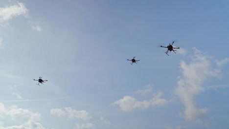 Three-Military-Drones-hovering-in-the-Air-against-blue-Sky-and-Clouds
