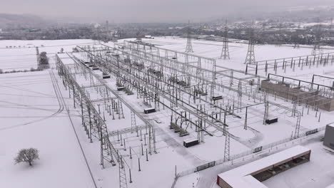 Electricity-power-distribution-station-in-snowy-winter-landscape,-drone-truck-shot