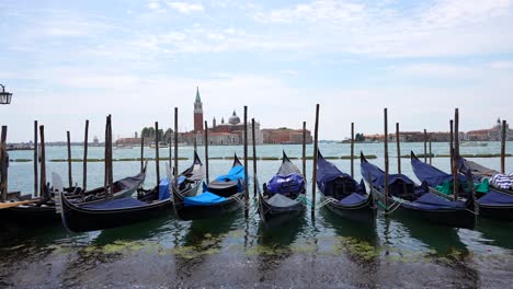 Woman-walking-by-gondolas-with-San-Giorgio-Maggiore-basilica-in-background,-Venezia