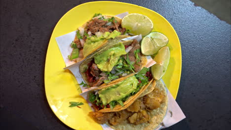 Slow-motion-overhead-shot-of-a-yellow-plastic-plate-with-a-variety-of-tacos-at-a-traditional-mexican-restaurant